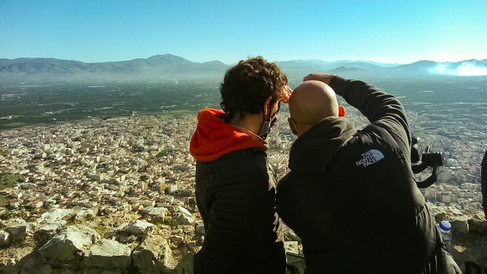 Film crew setting up camera equipment in historic Greek location